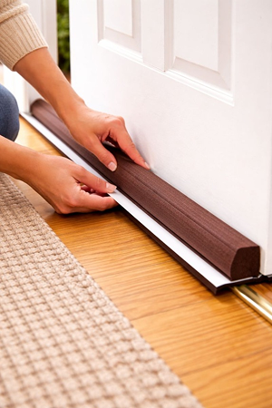 Hands fitting a dark timber draught excluder strip along the bottom of an internal door