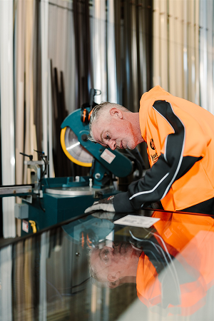 Worker in branded hi-vis inspecting the surface of a large double glazed glass panel in the workshop