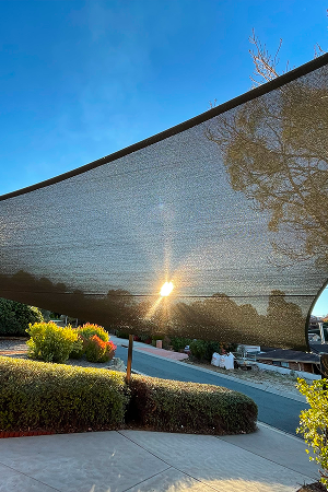 Large shade sail stretched over a driveway and garden with the low sun shining behind it