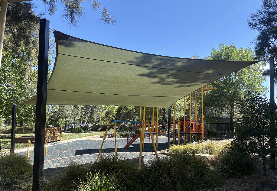 Beige shade sail on steel posts shading a children's playground on a sunny day