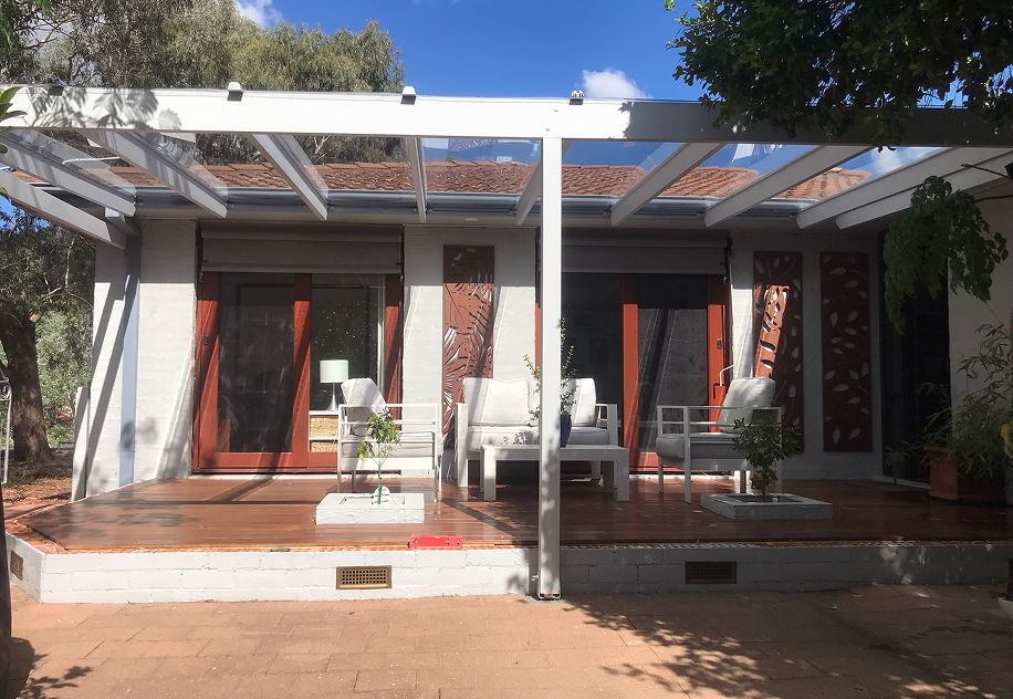 Clear polycarbonate roofing over a white timber pergola shading a patio with outdoor lounge seating