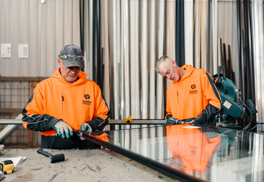 Two workers assembling a double glazed window unit on the bench in the fabrication workshop