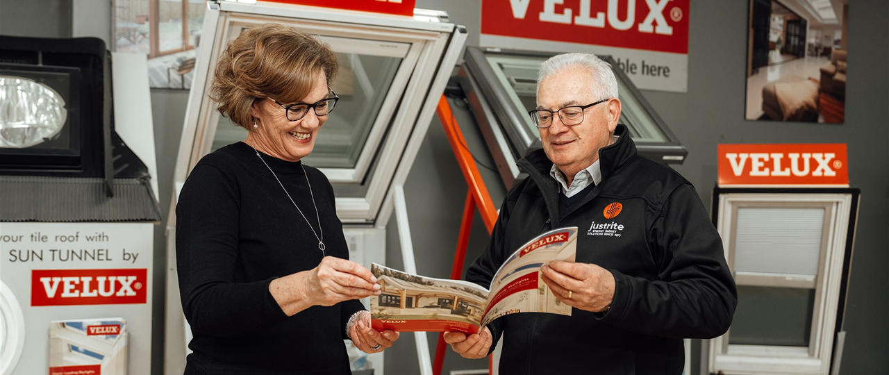 Two people looking through a VELUX brochure in a showroom lined with VELUX skylight displays
