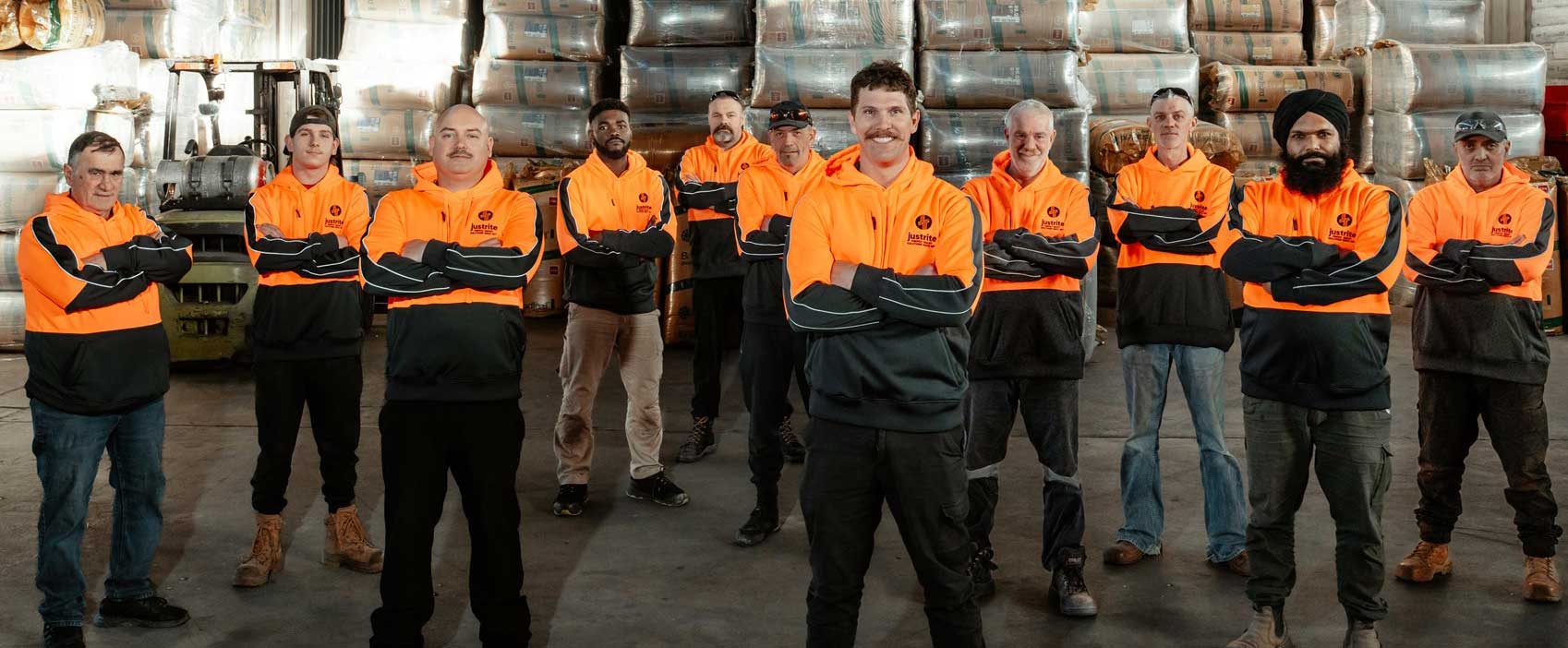 Team of installers in orange hi-vis standing in the warehouse in front of stacked insulation
