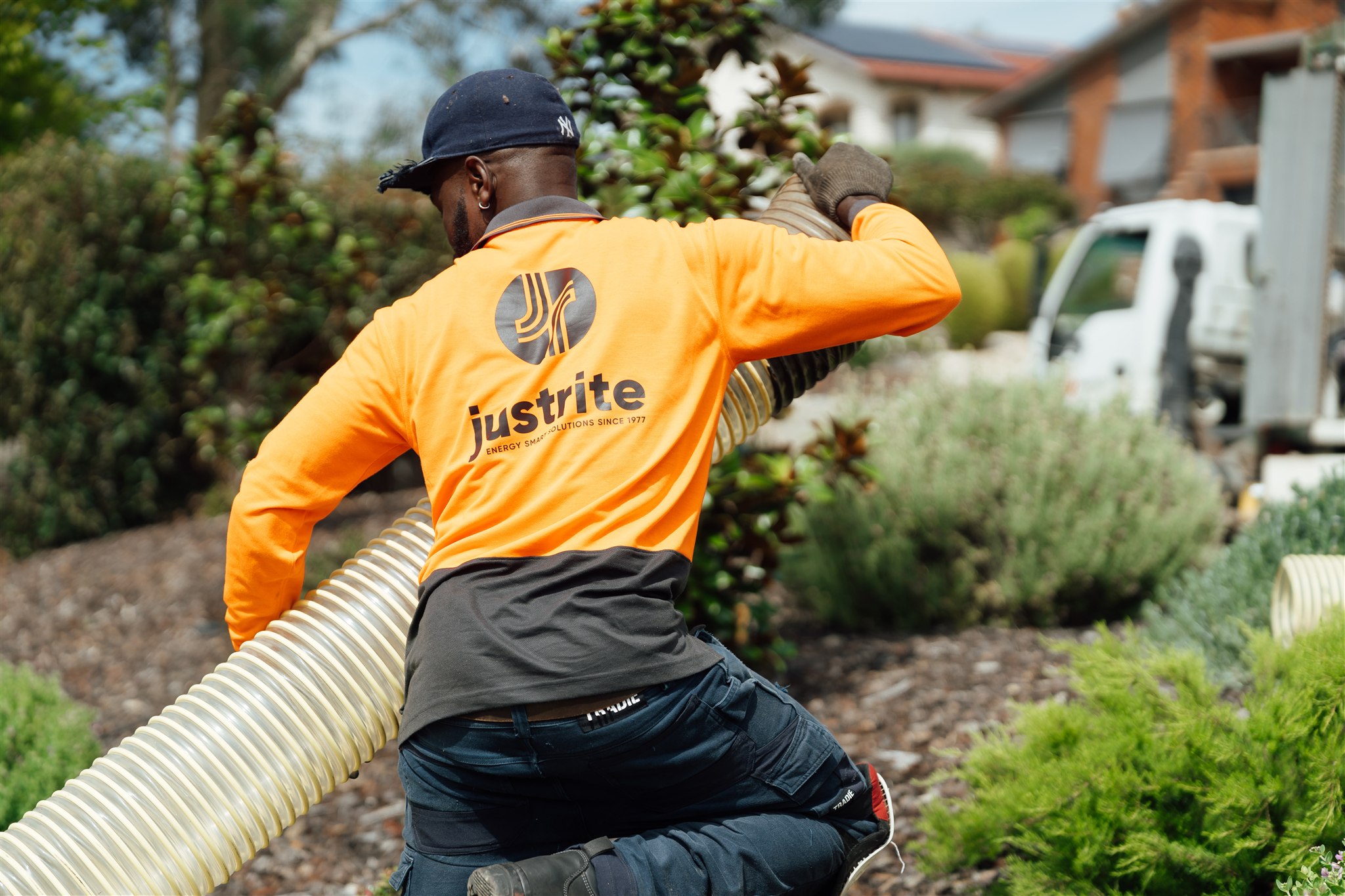 Installer in Just Rite hi-vis carrying an insulation blowing hose from the truck to a house