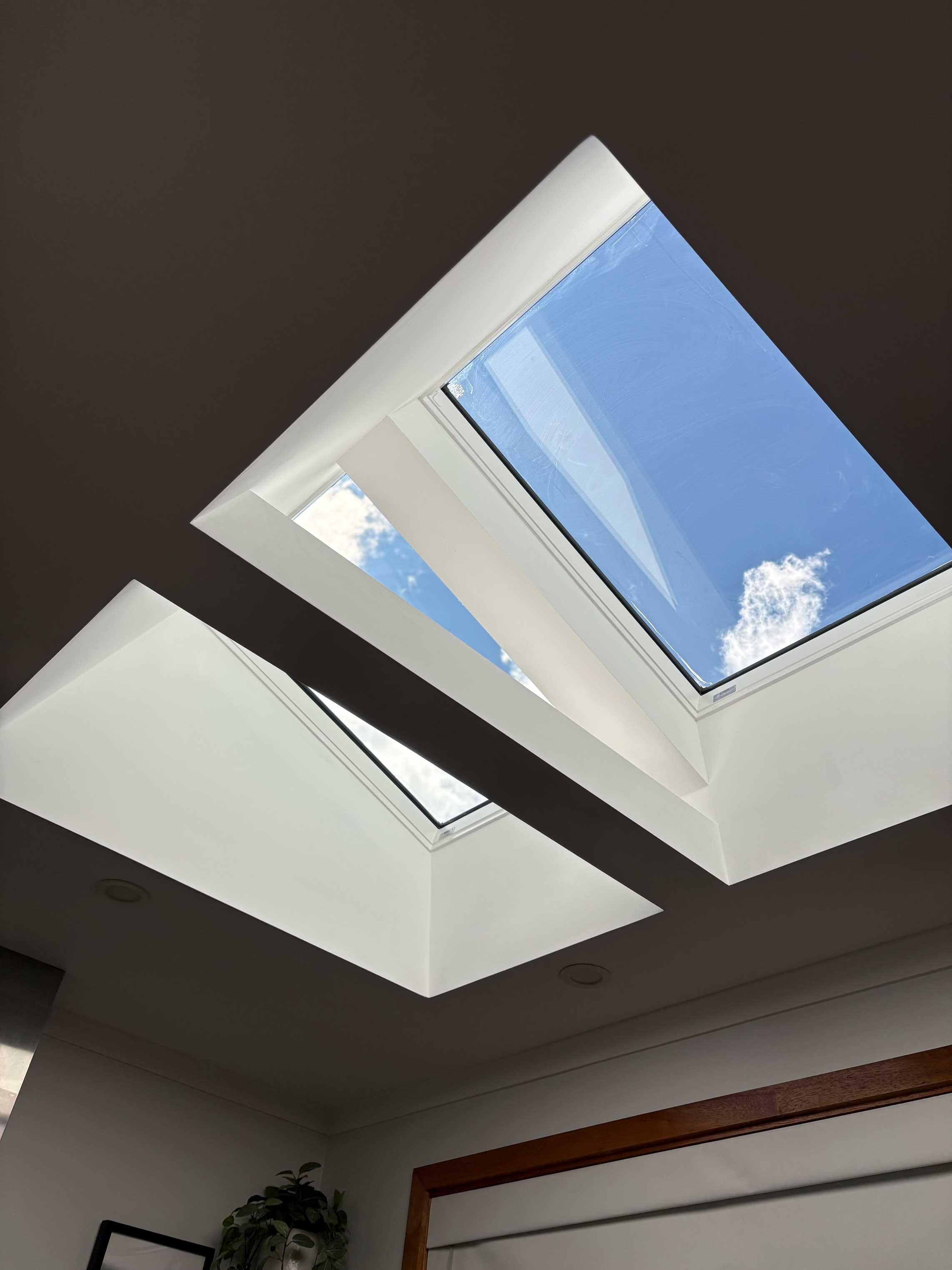 Two skylights fitted into a raked ceiling, showing blue sky above