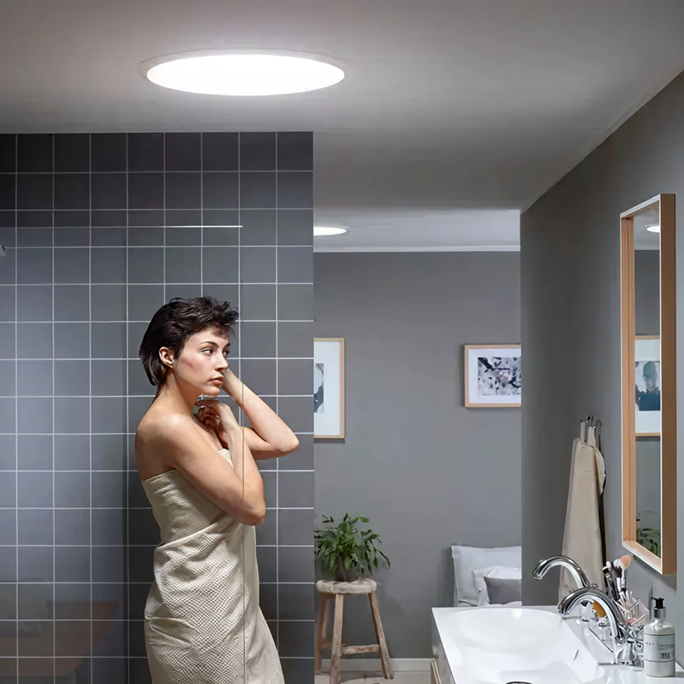 Round sun tunnel skylight lighting a grey-tiled bathroom from the ceiling