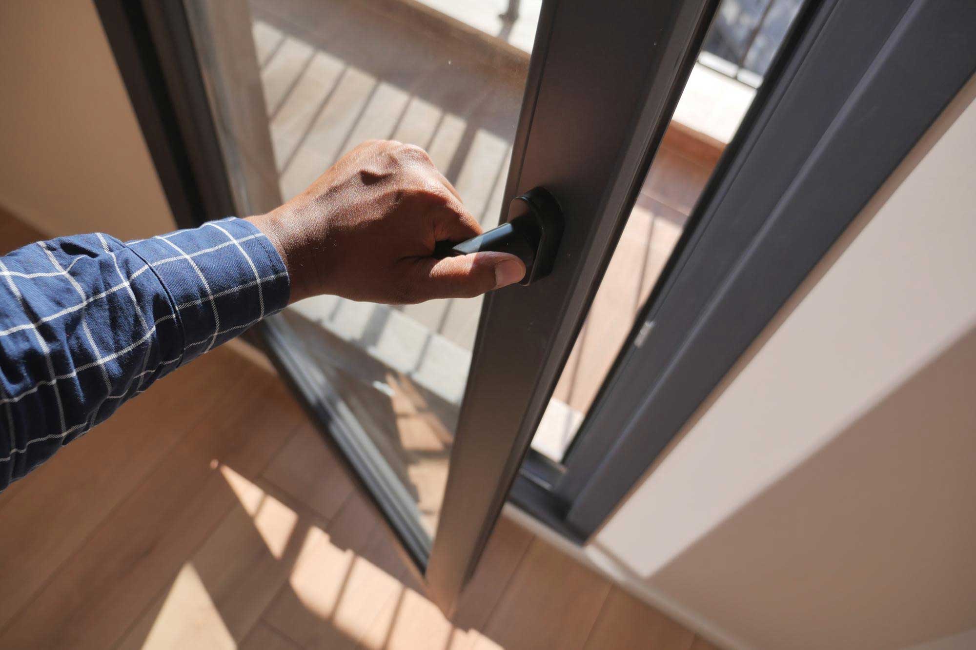 Hand opening the latch of an aluminium framed sliding glass door
