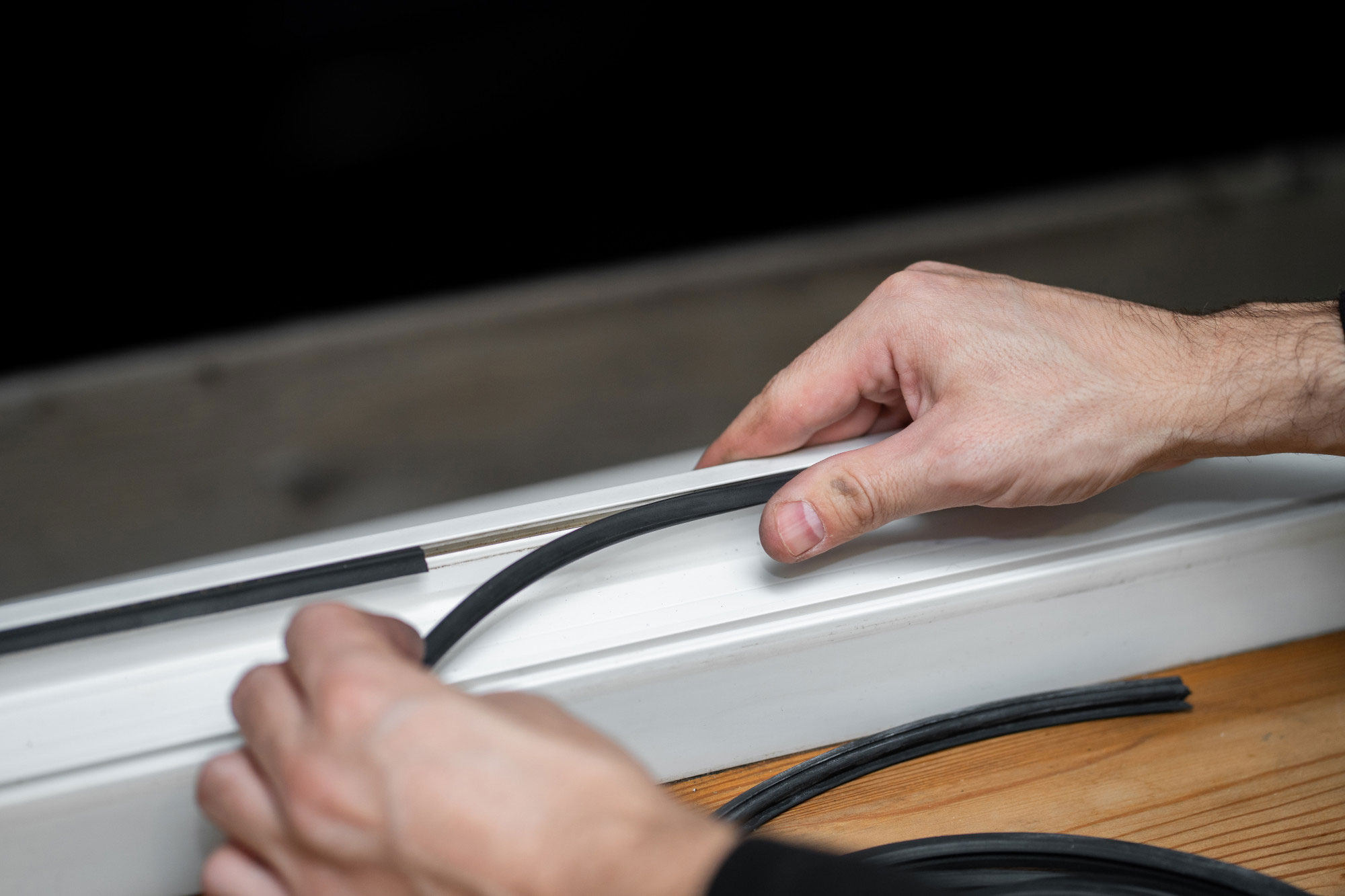 Hands pressing a rubber draught seal strip into the frame of a white window