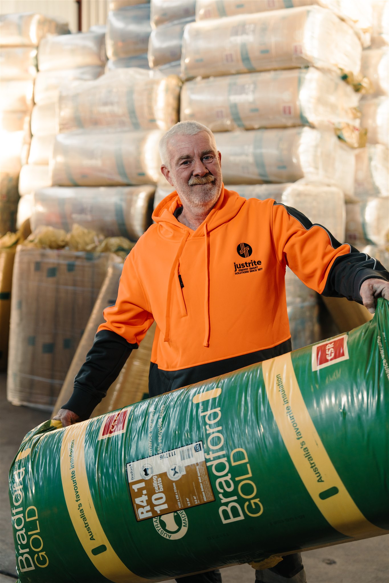 Worker in a Just Rite hoodie carrying a bag of Bradford Gold R4.1 insulation in the warehouse