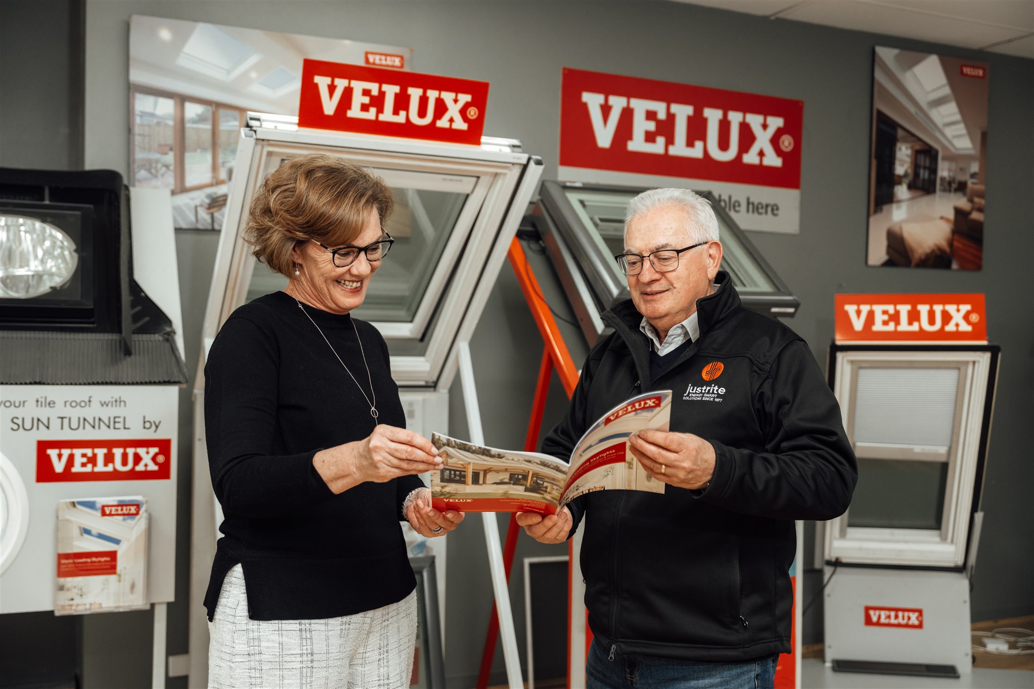 Two people looking through a brochure in a showroom displaying VELUX skylights and roof windows