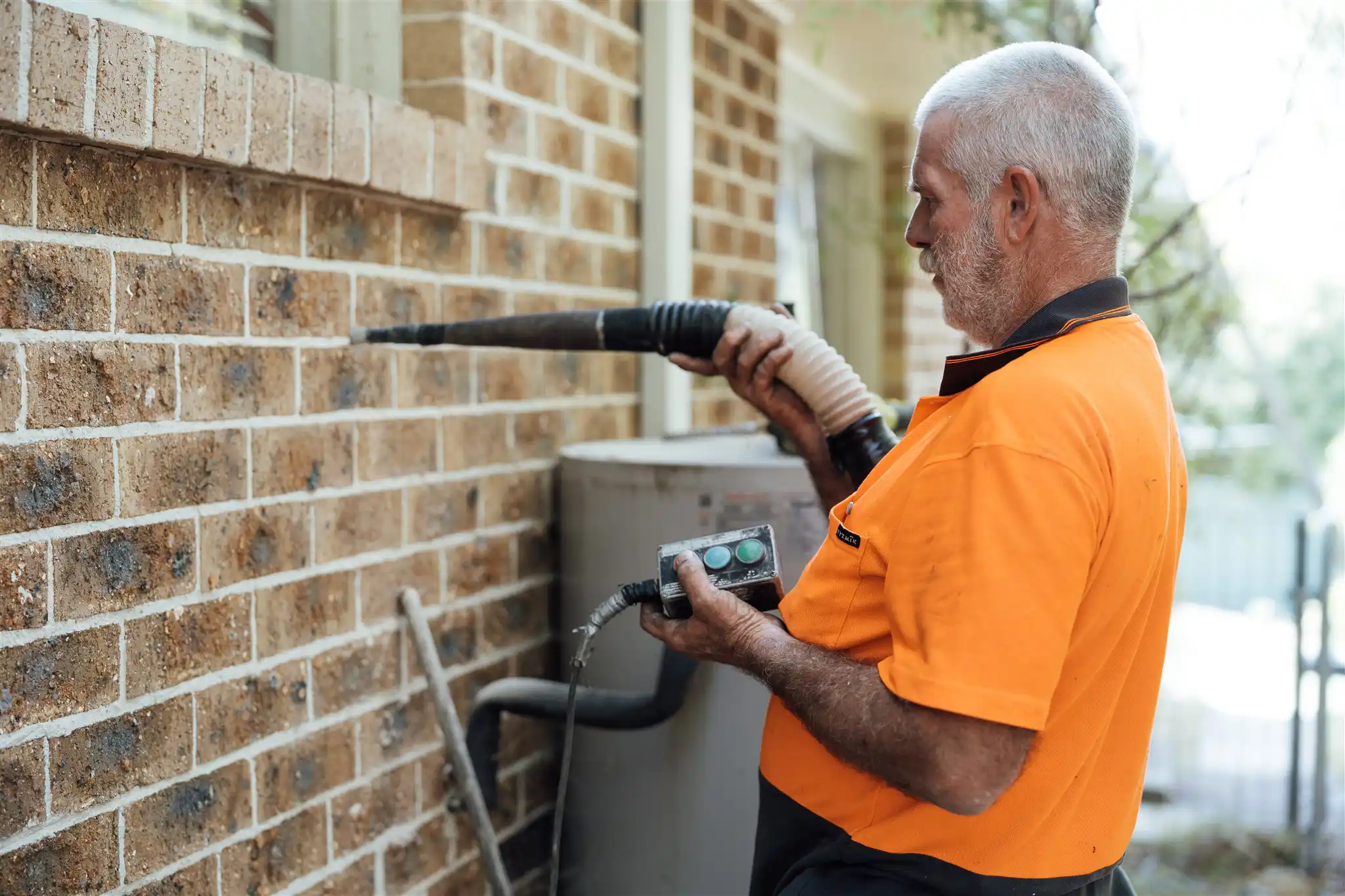 Worker in hi-vis drilling into an external brick wall using a dust-extraction drill