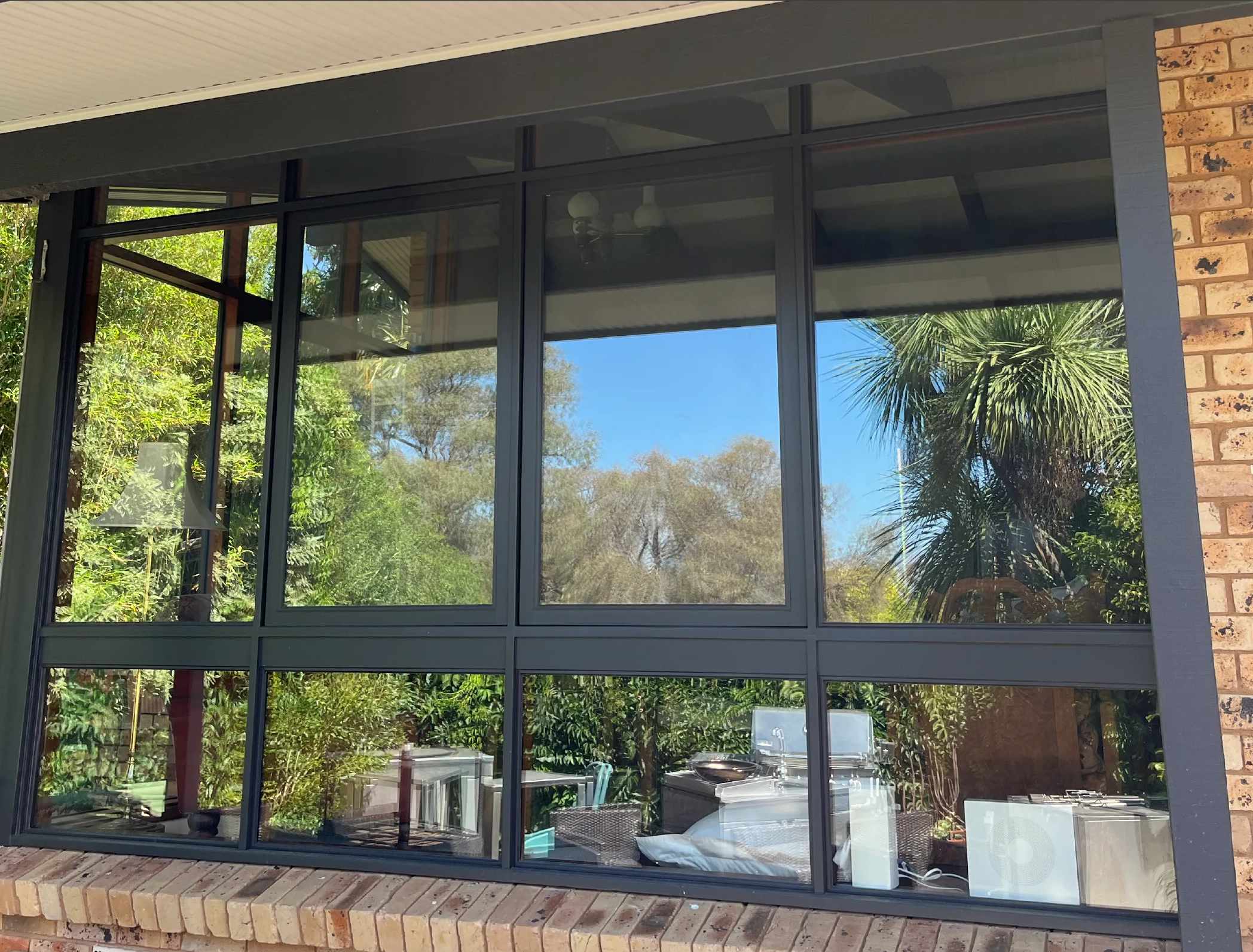 Charcoal aluminium double glazed windows above a brick sill, with garden and blue sky reflected in the glass
