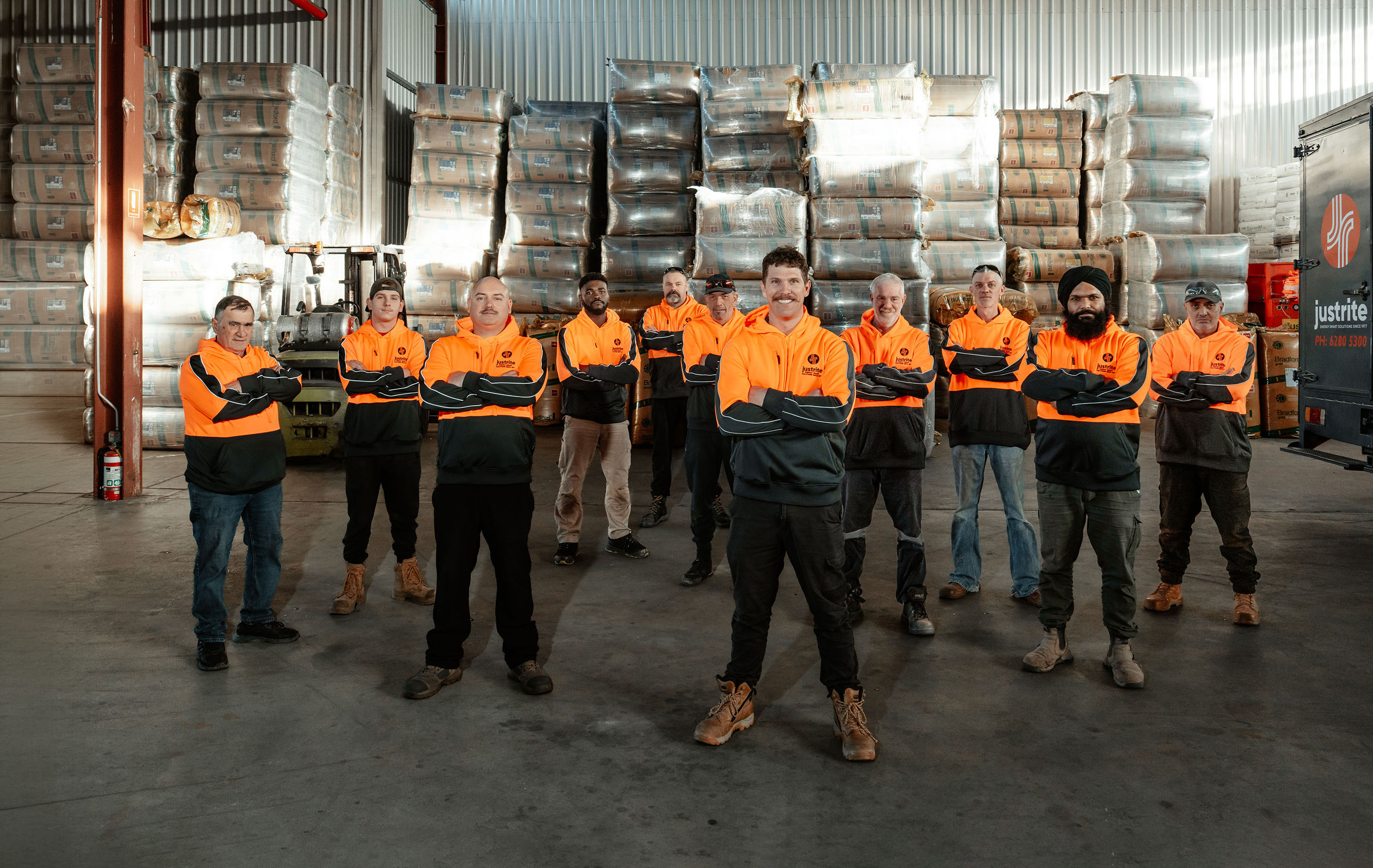 Just Rite team in hi-vis workwear standing in the warehouse in front of stacked insulation and a branded van