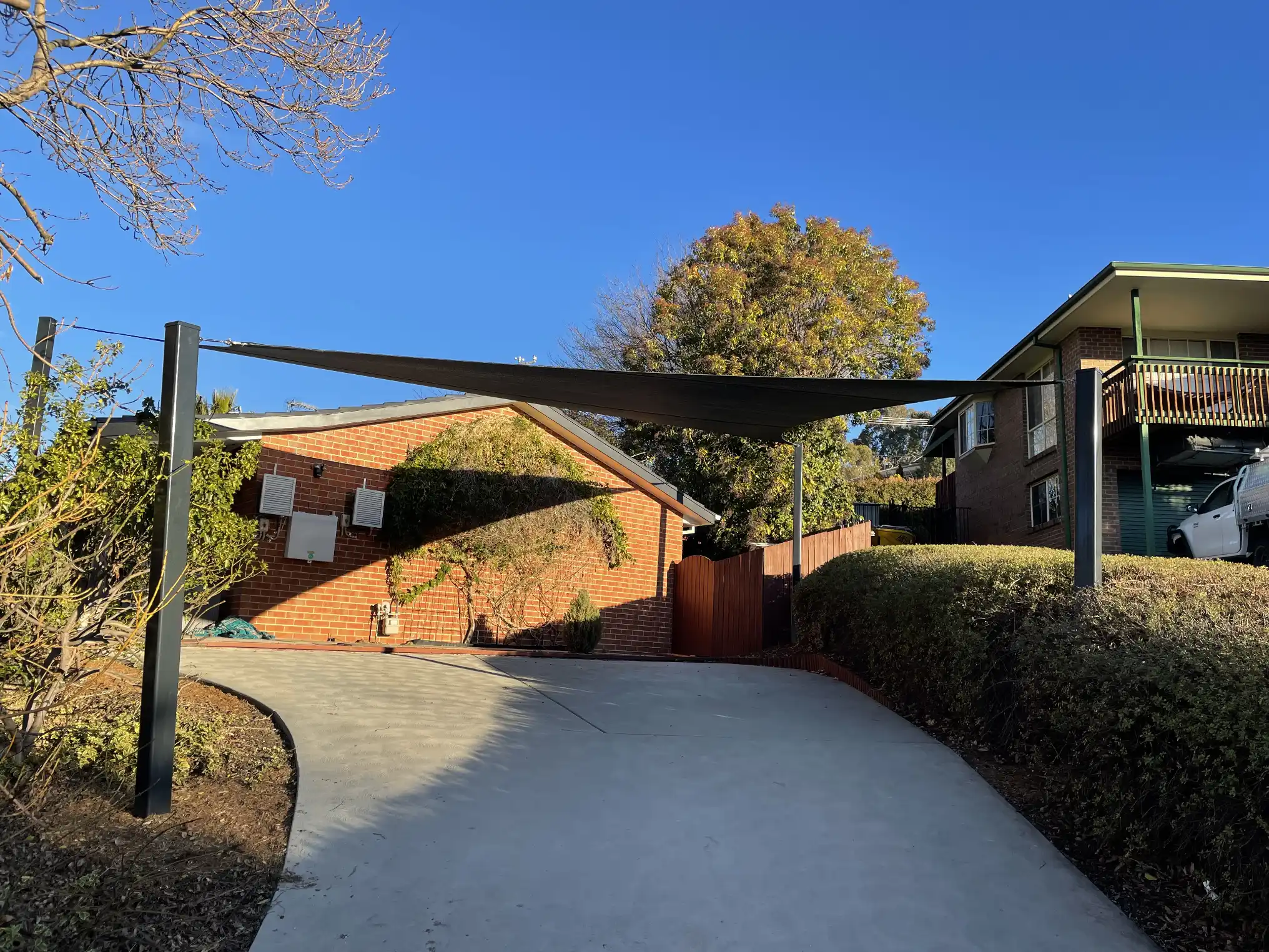 Charcoal shade sail installed as a carport over a driveway beside a brick home