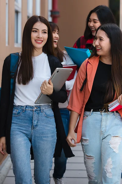 Two graduates in green gowns reviewing documents together and smiling outside a building.