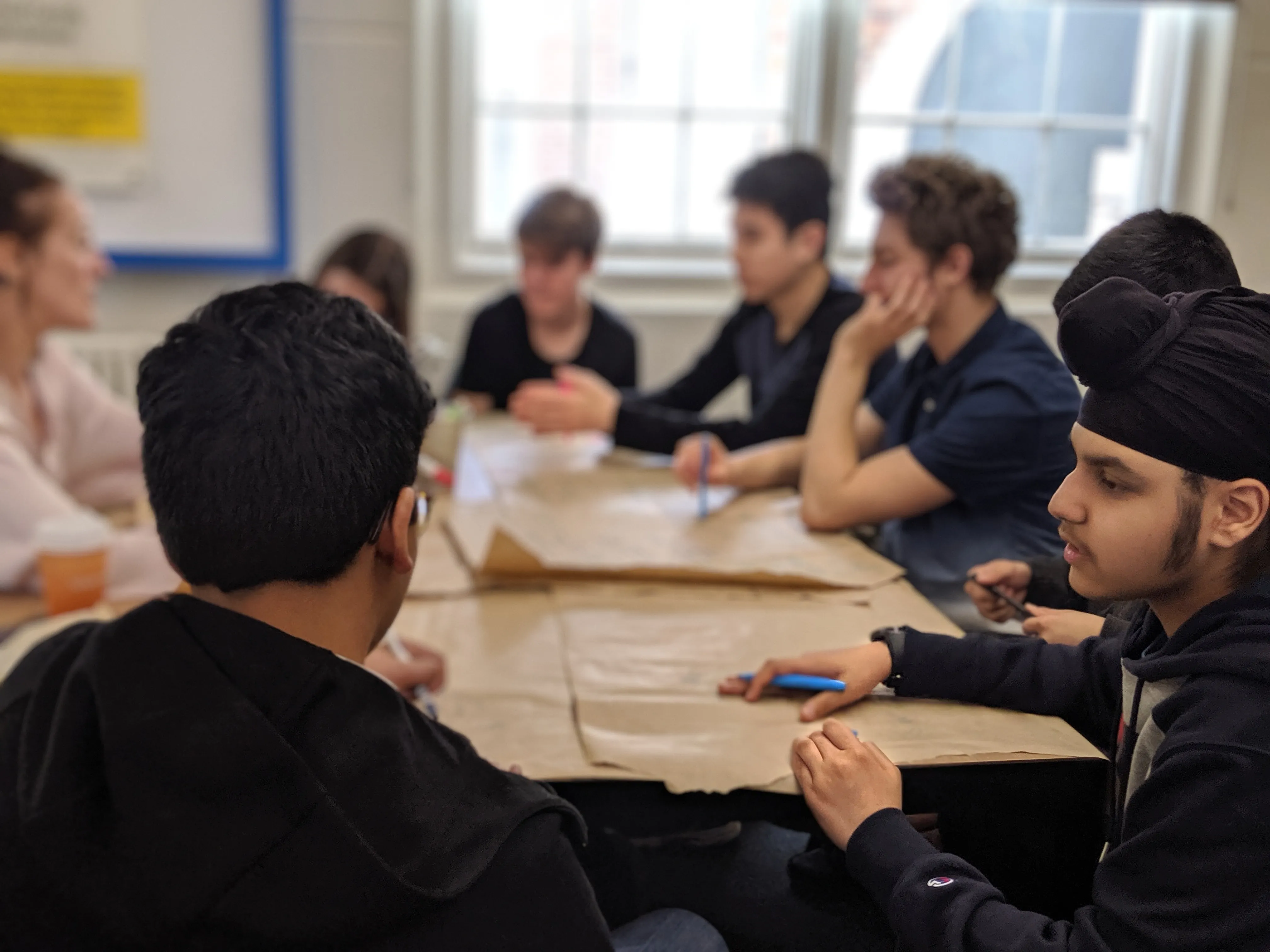 Five diverse students study together at a round table with books and a laptop in a library.