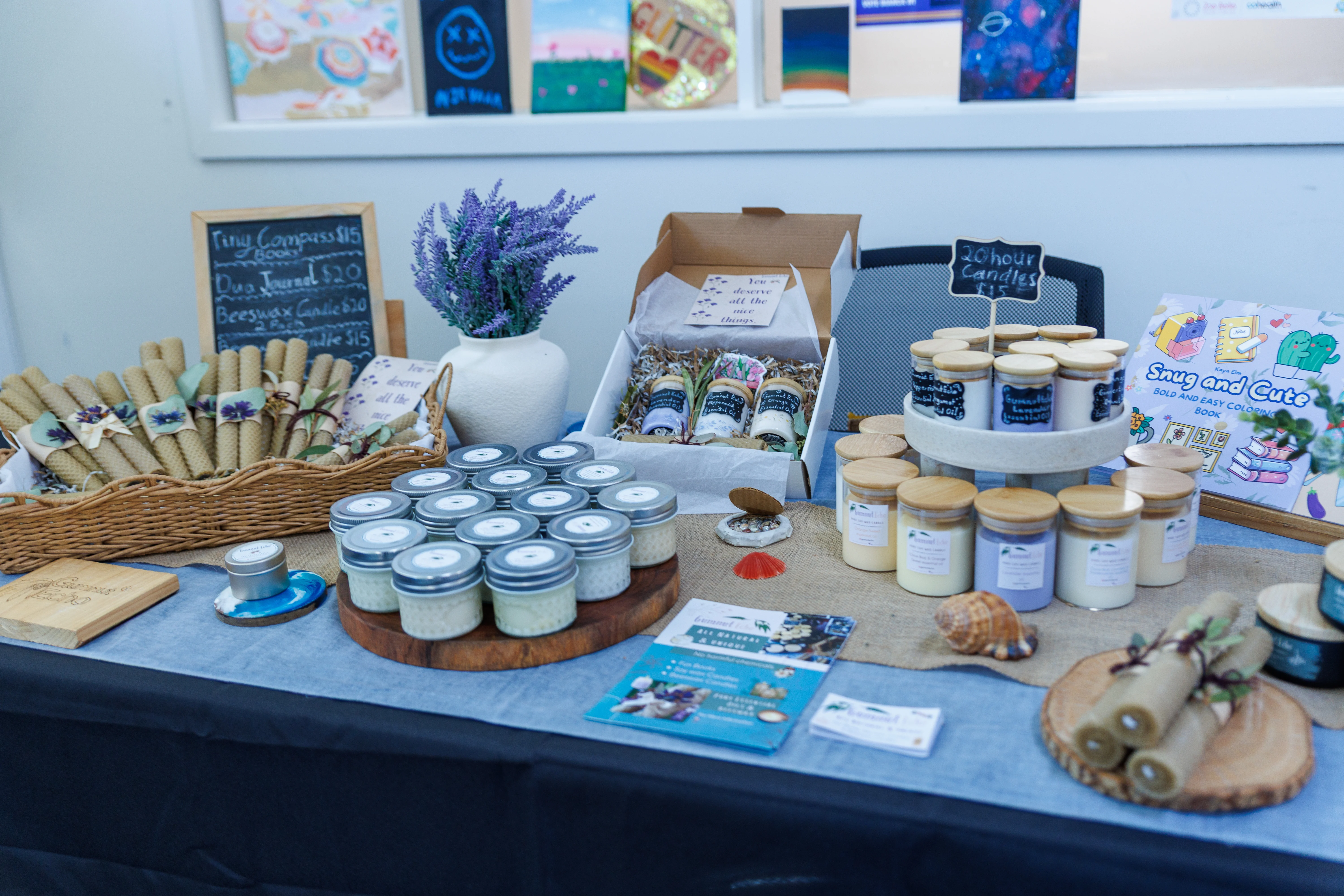 Table display of handmade candles, rolled beeswax candles, lavender bouquet, and a coloring book.