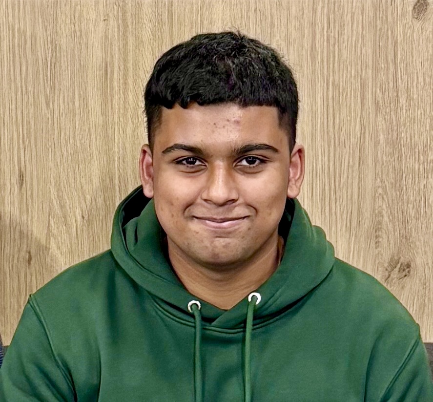 Young man with short black hair wearing a green hoodie against a wood-textured background.