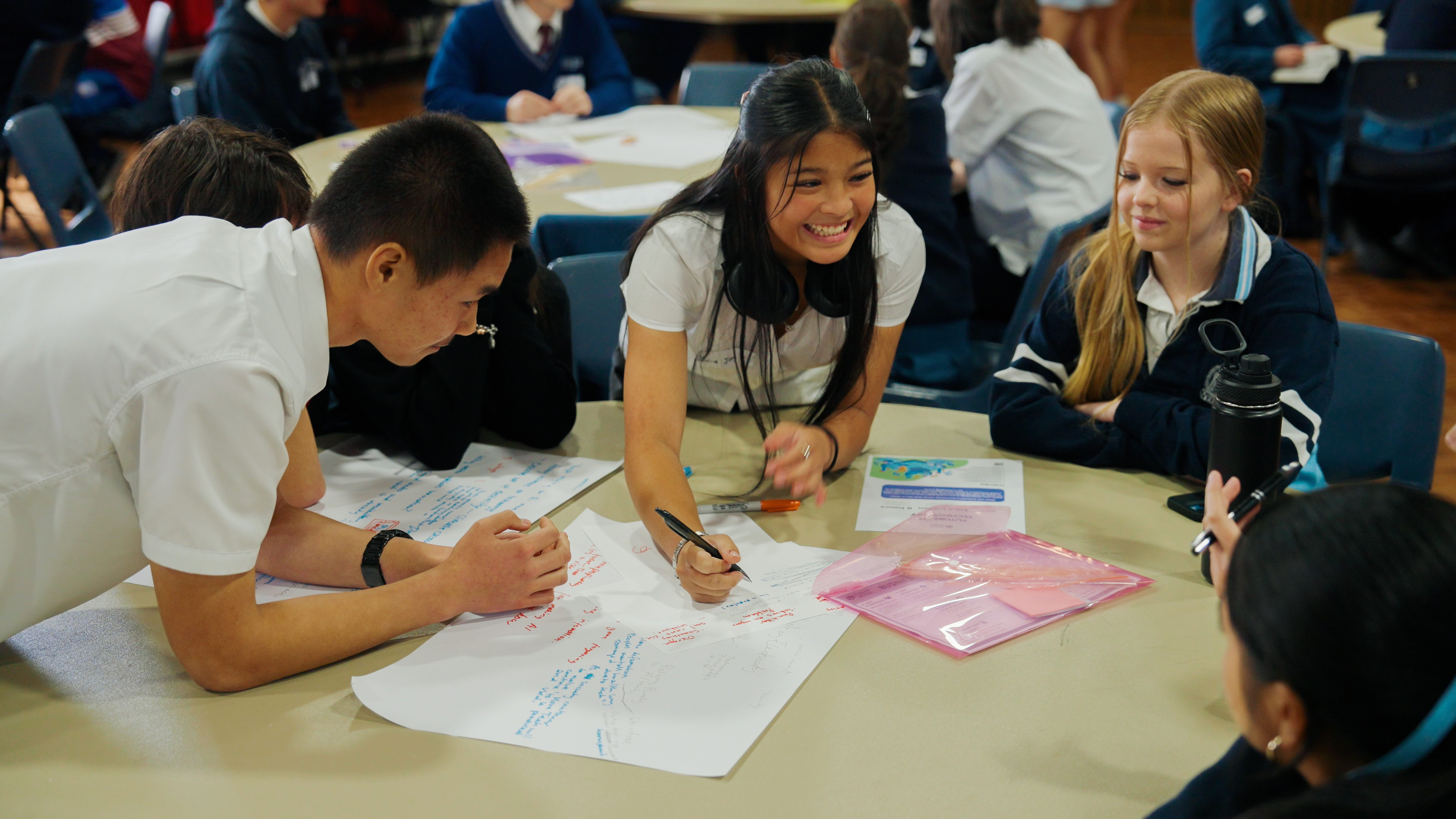 Five students studying together at a round table with books and a laptop in a library.