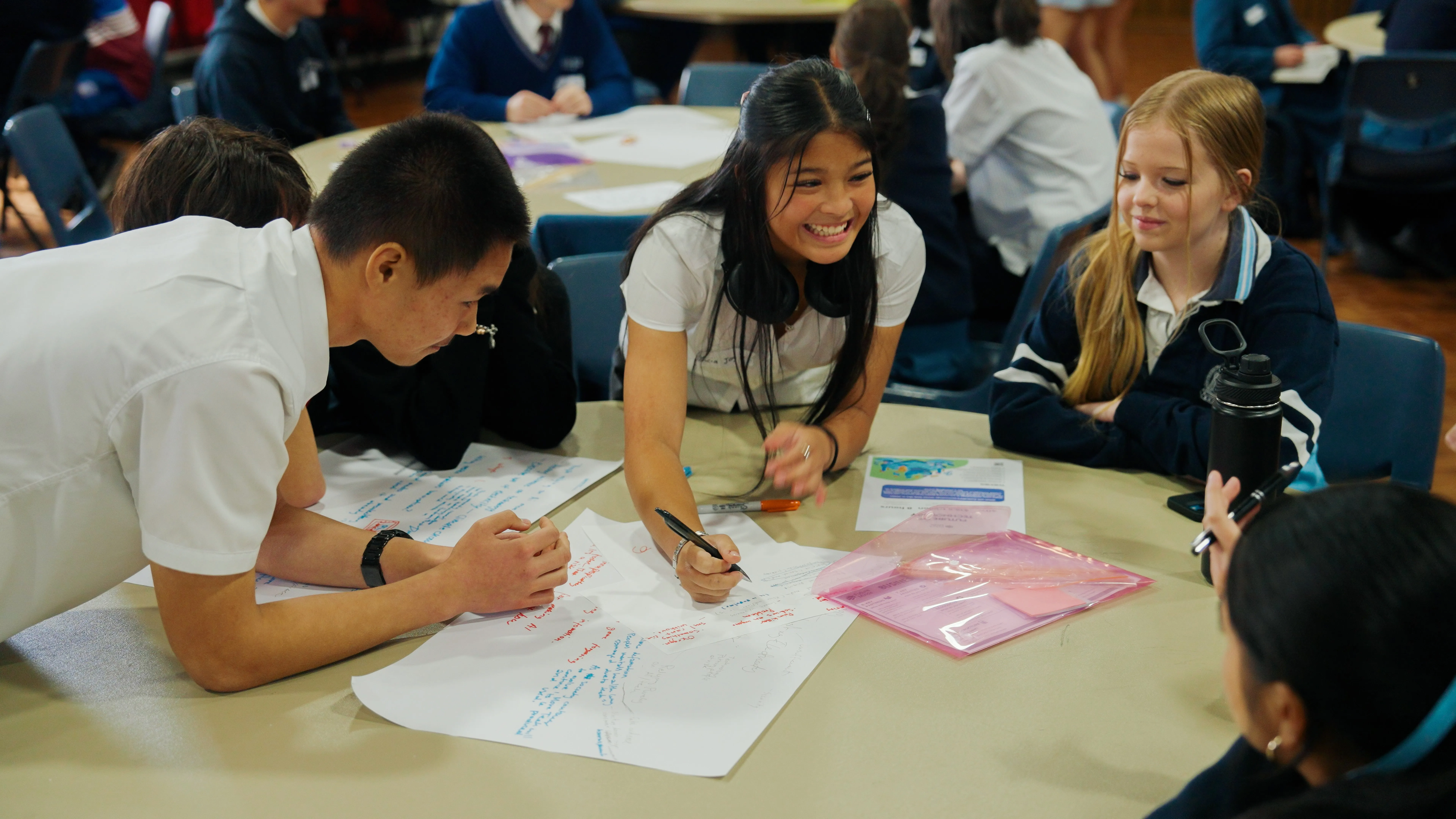 Group of students in classroom collaborating on a project with papers and pens on the table.