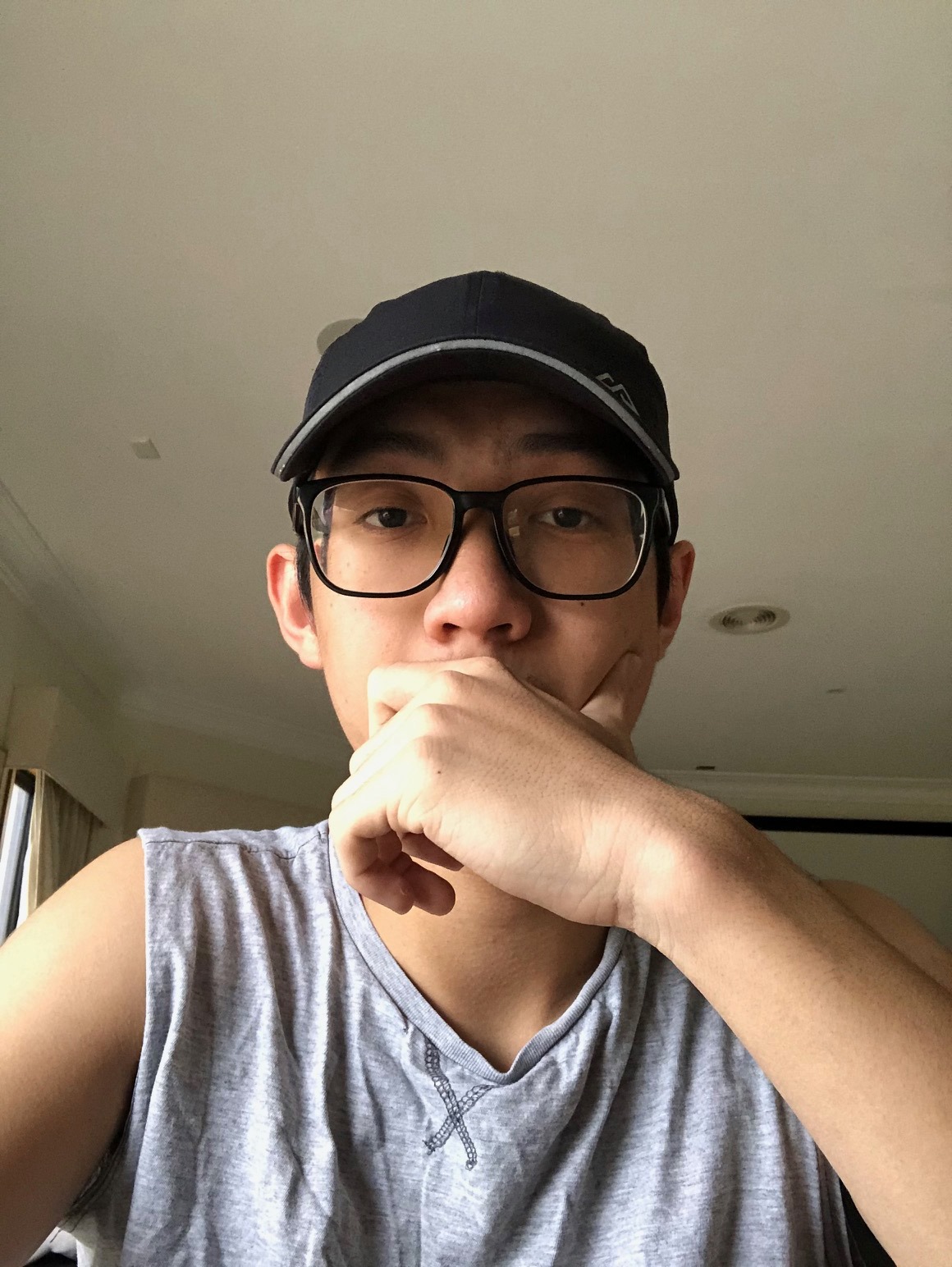Young man wearing glasses and a black cap, resting his chin on his hand, indoors.
