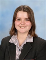 Smiling young woman with shoulder-length brown hair wearing a school uniform with a checkered collar.