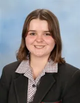 Smiling young woman with shoulder-length brown hair wearing a school uniform with a checkered collar.