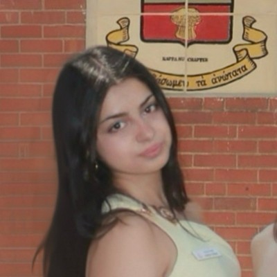 Young woman with long dark hair posing in front of a brick wall with a crest emblem.