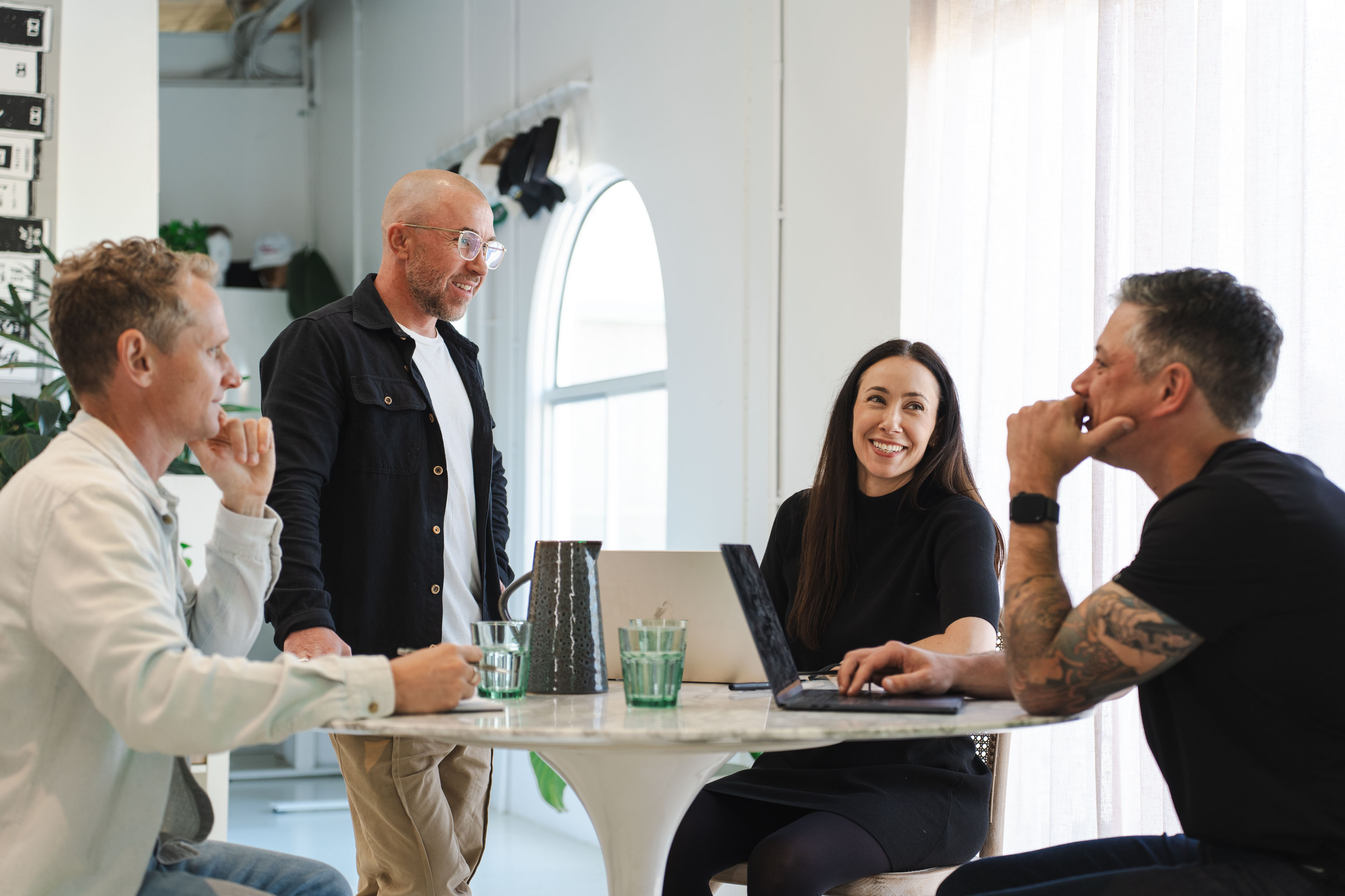 Four members of the New Beach team laughing around a round table in the sunlit Byron Bay office