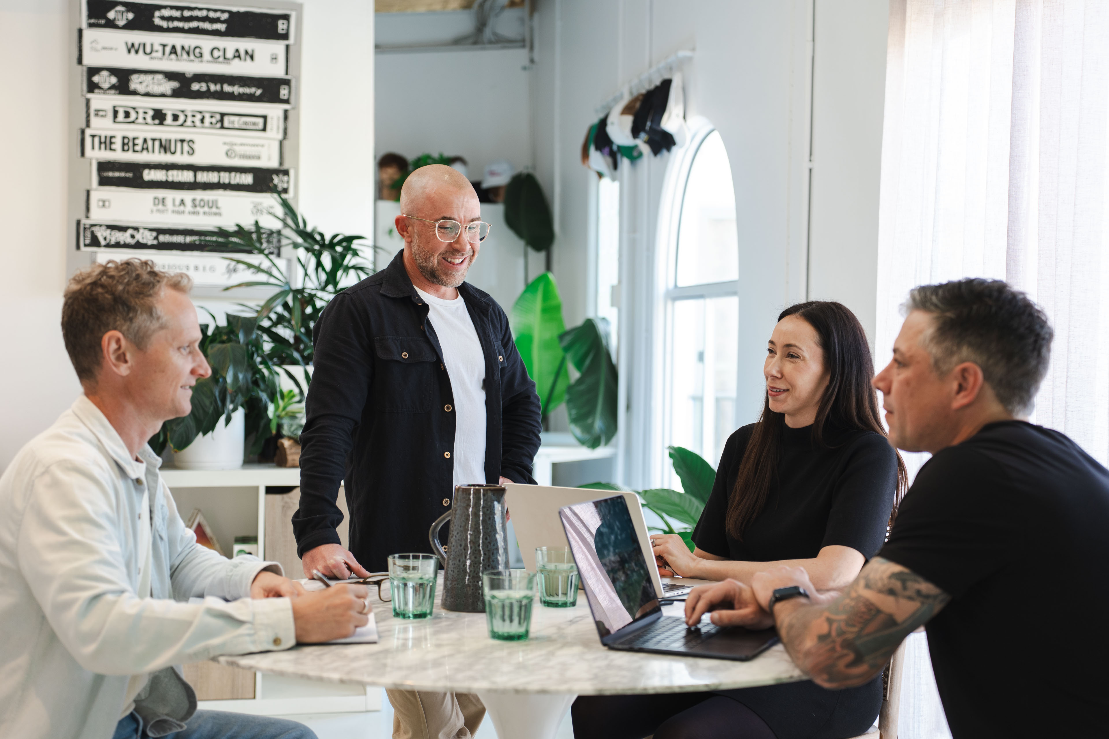 Four New Beach team members meeting around a table, with cassette tapes and plants lining the office shelves