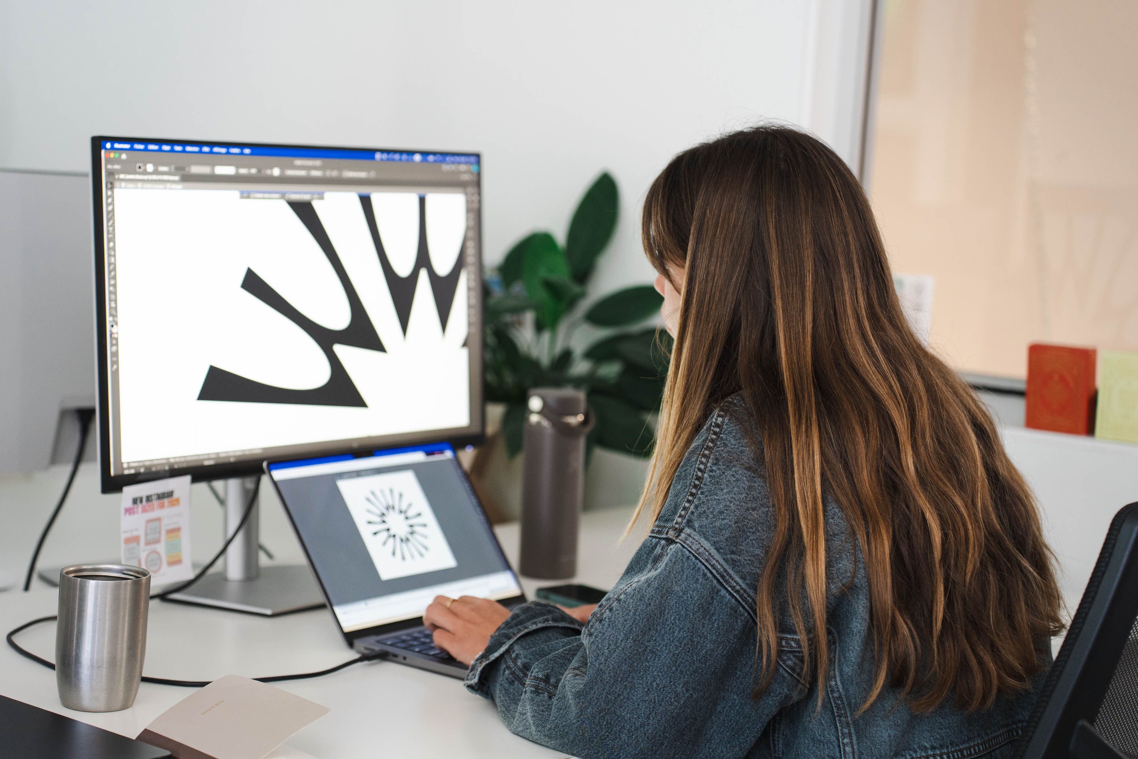A member of the New Beach team editing a black graphic mark on a large monitor at a desk in the Byron Bay office