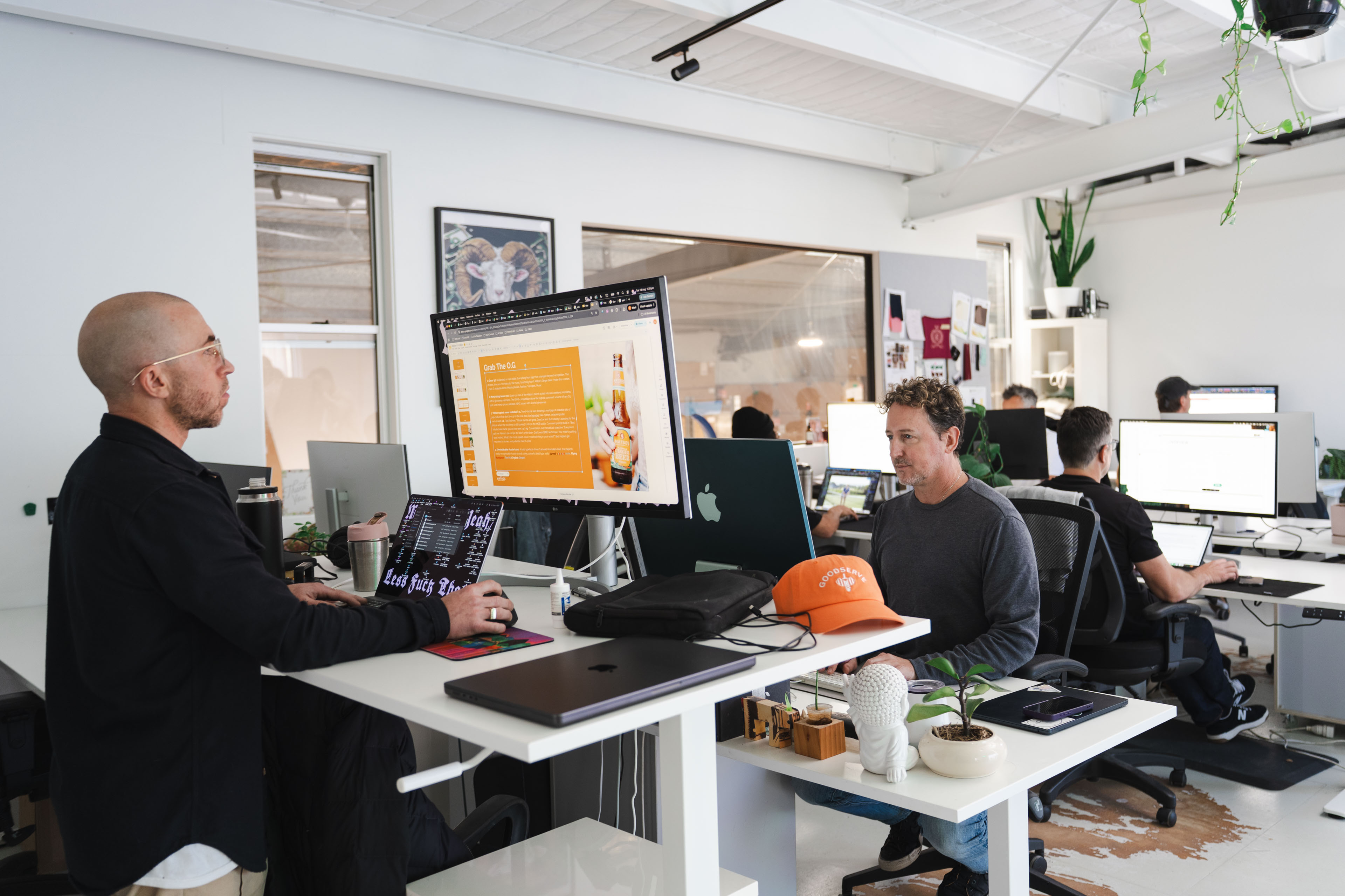 Two New Beach team members talking across desks in the open plan Byron Bay studio while others work behind them