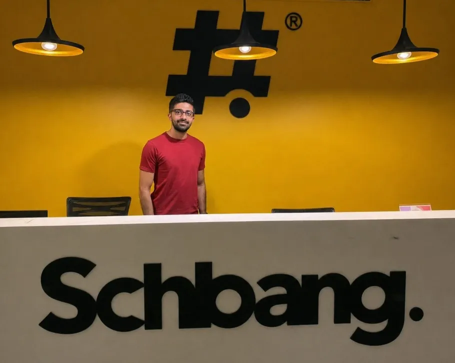 Akshay Gurnani standing beside a wall-mounted Schbang logo, the independent agency he co-founded.
