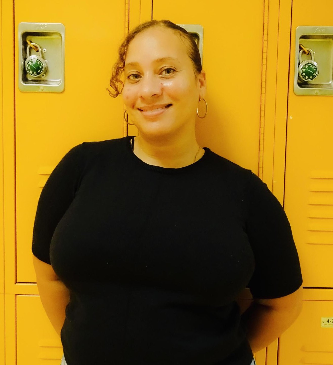 Staff member Indira Kemp smiling in front of yellow school lockers