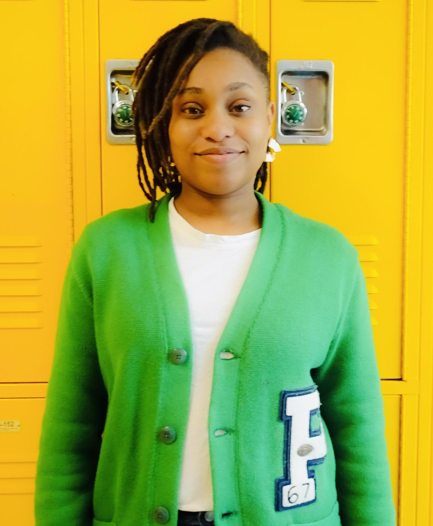 Kyanna Louissaint smiling in green letterman cardigan by school lockers