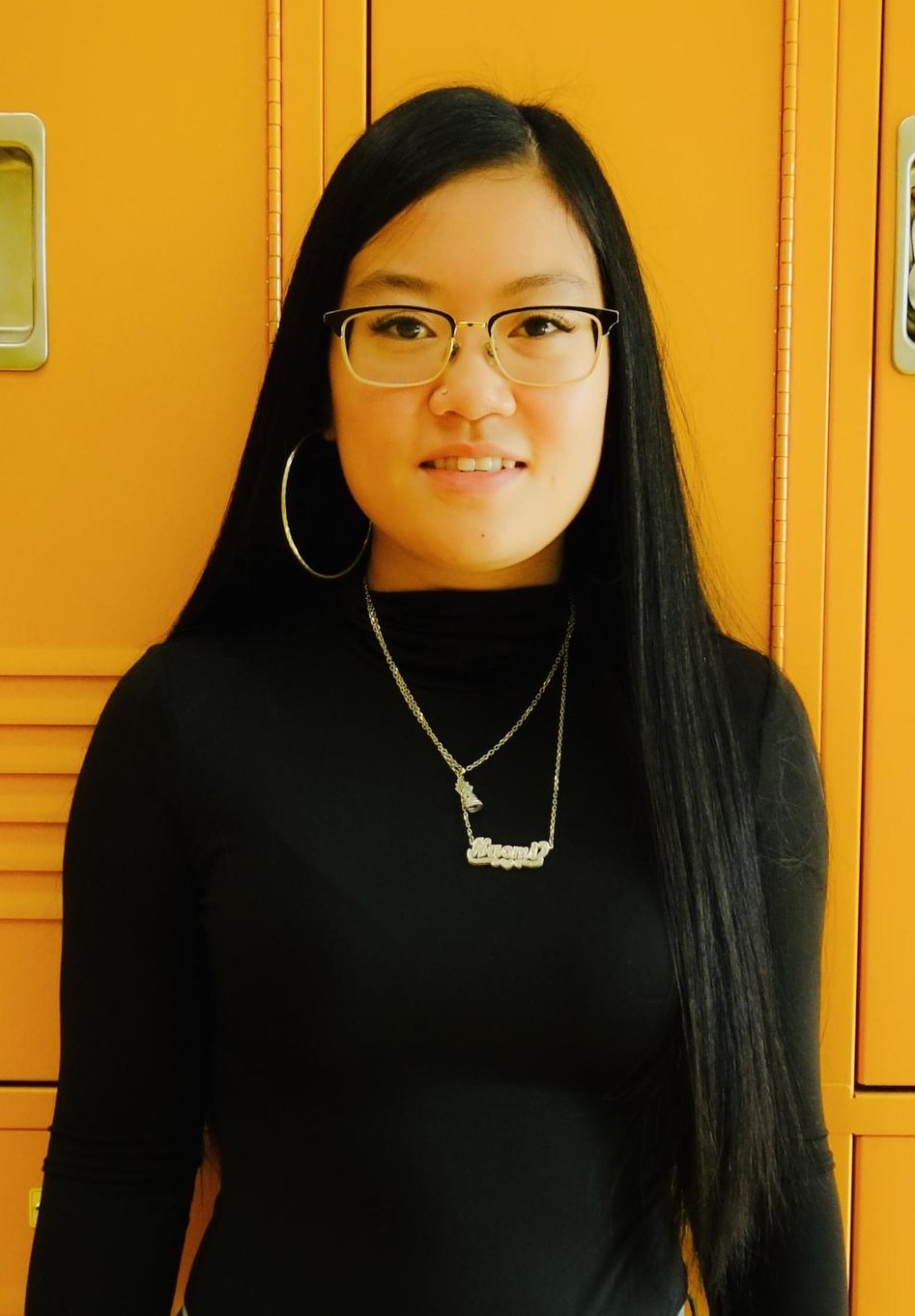 Naomi Tsao smiling in front of yellow school lockers