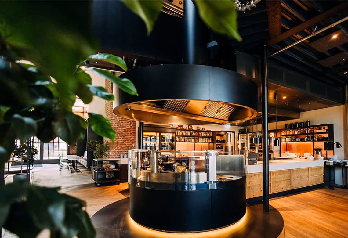 Modern restaurant interior with a central circular kitchen island and wooden flooring.
