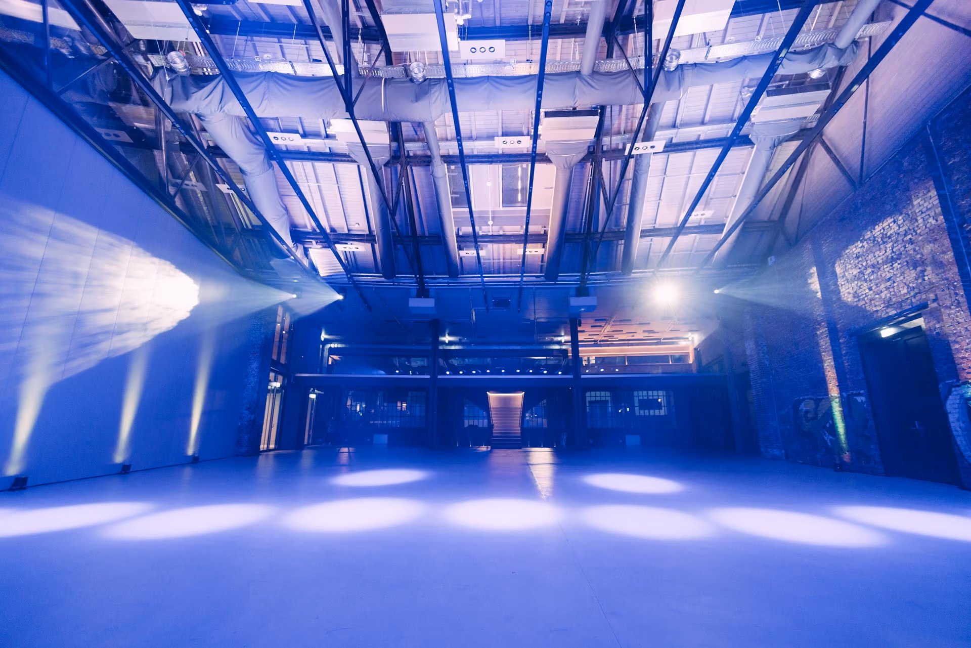 Empty industrial event space lit with blue lights and spotlights on floor and walls.