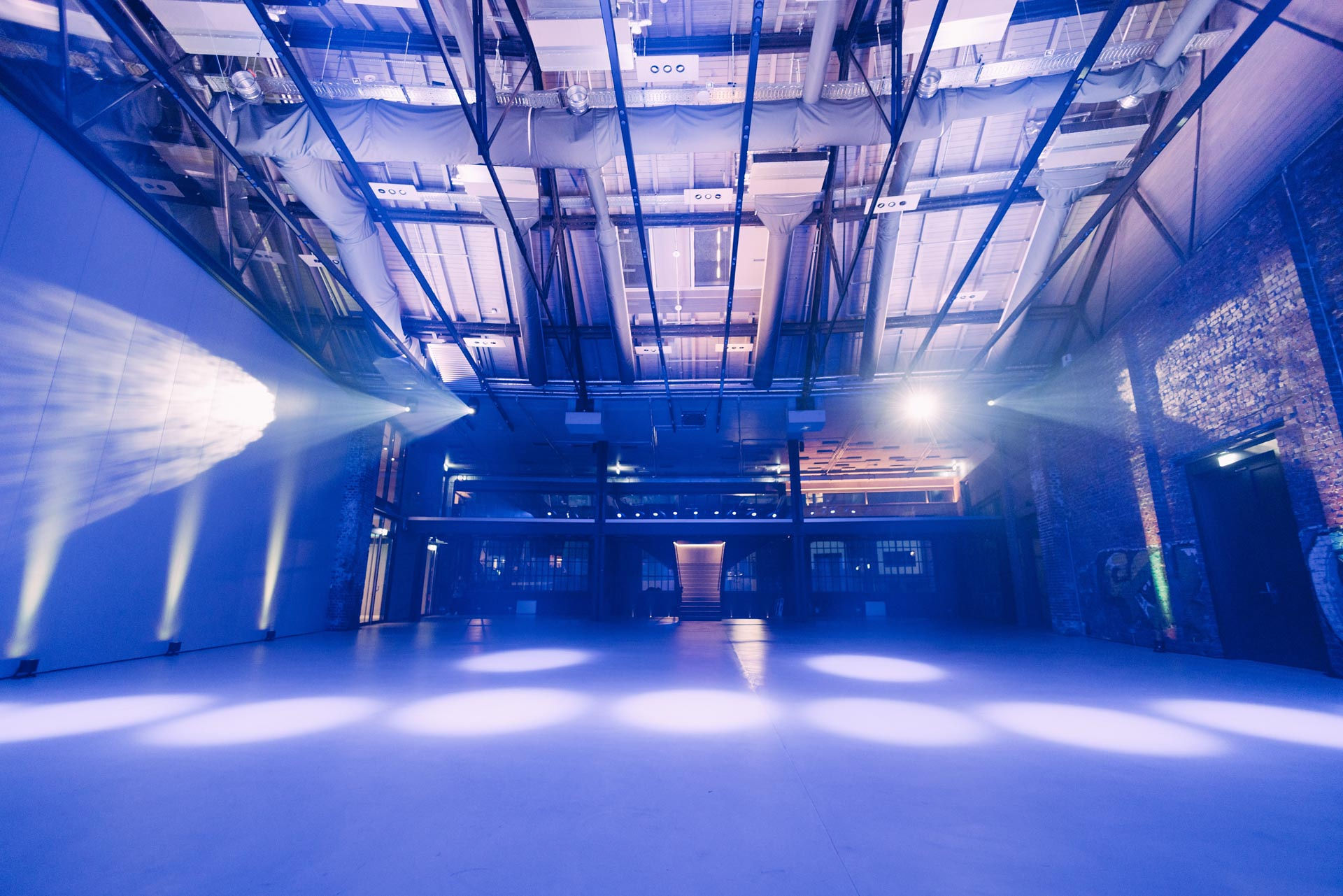 Empty industrial event space lit with blue lights and spotlights on floor and walls.