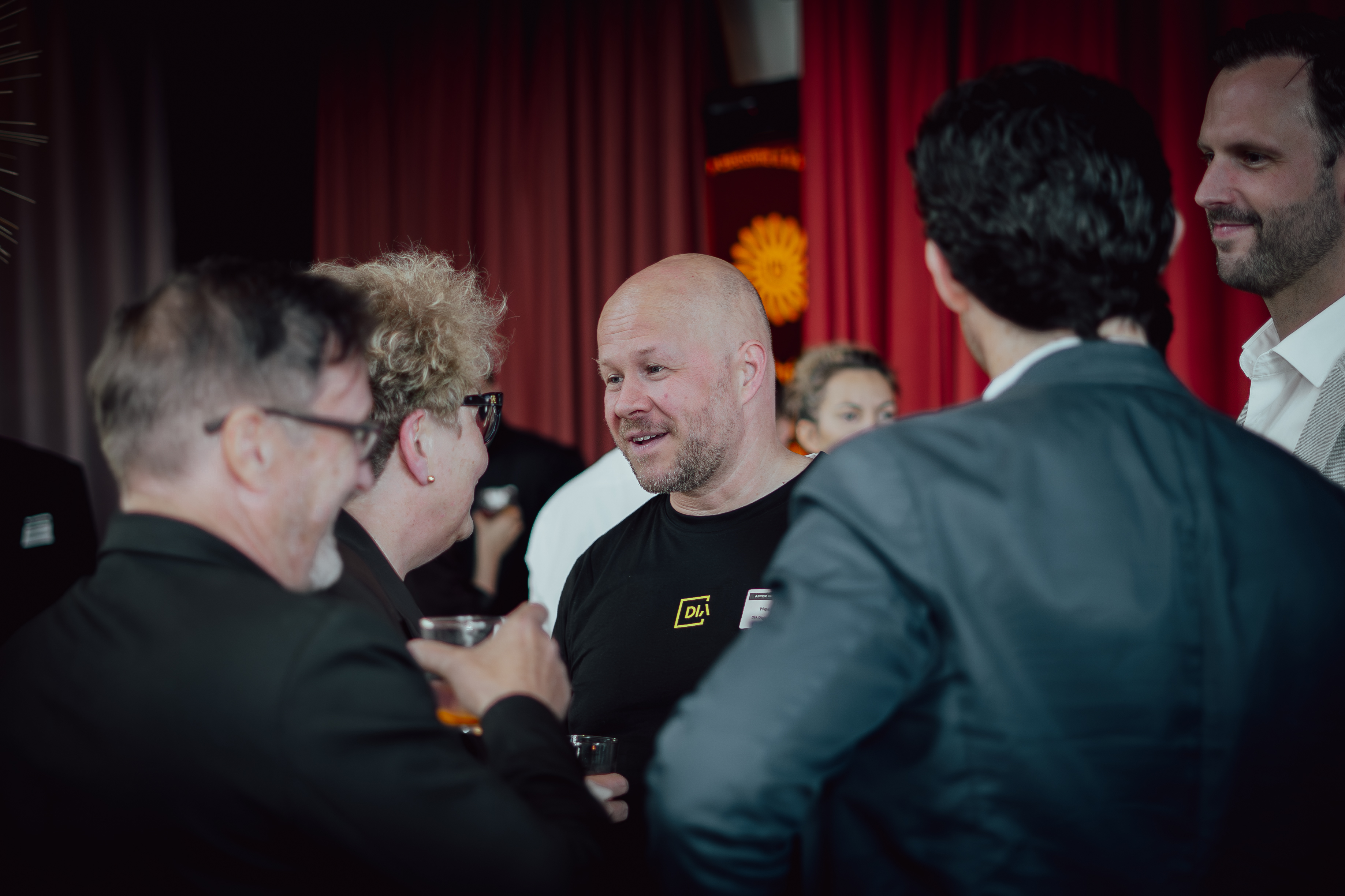 Group of people in conversation at an indoor event with red curtains in the background.