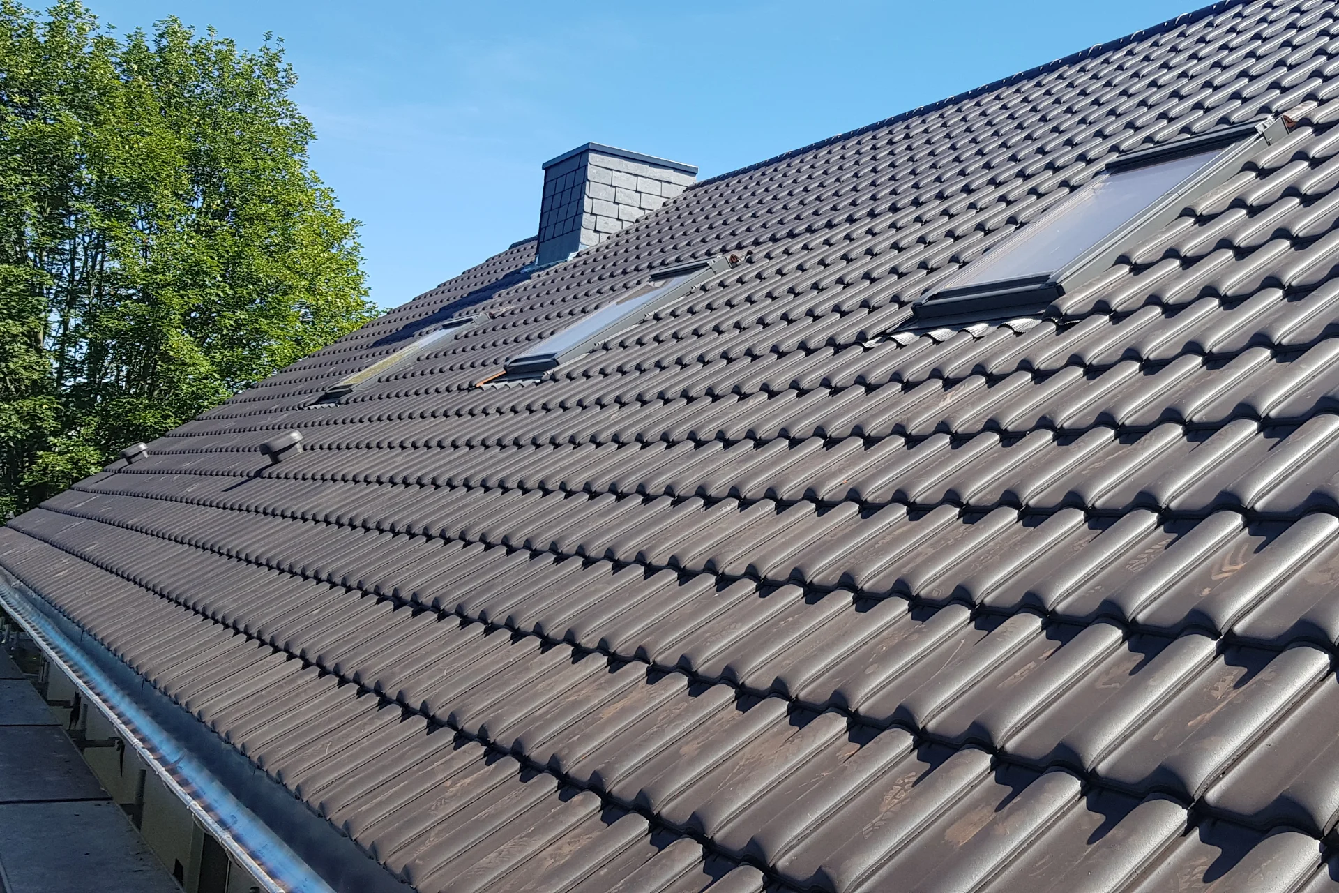 Neu eingedeckte Dachfläche mit dunklen Dachsteinen und Schneefanggitter unter blauem Himmel