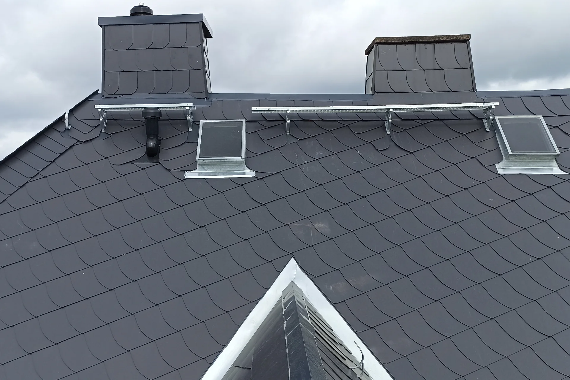 Fertiges Schieferdach mit VELUX-Dachfenstern, verschieferten Kaminen und Schneefanggitter