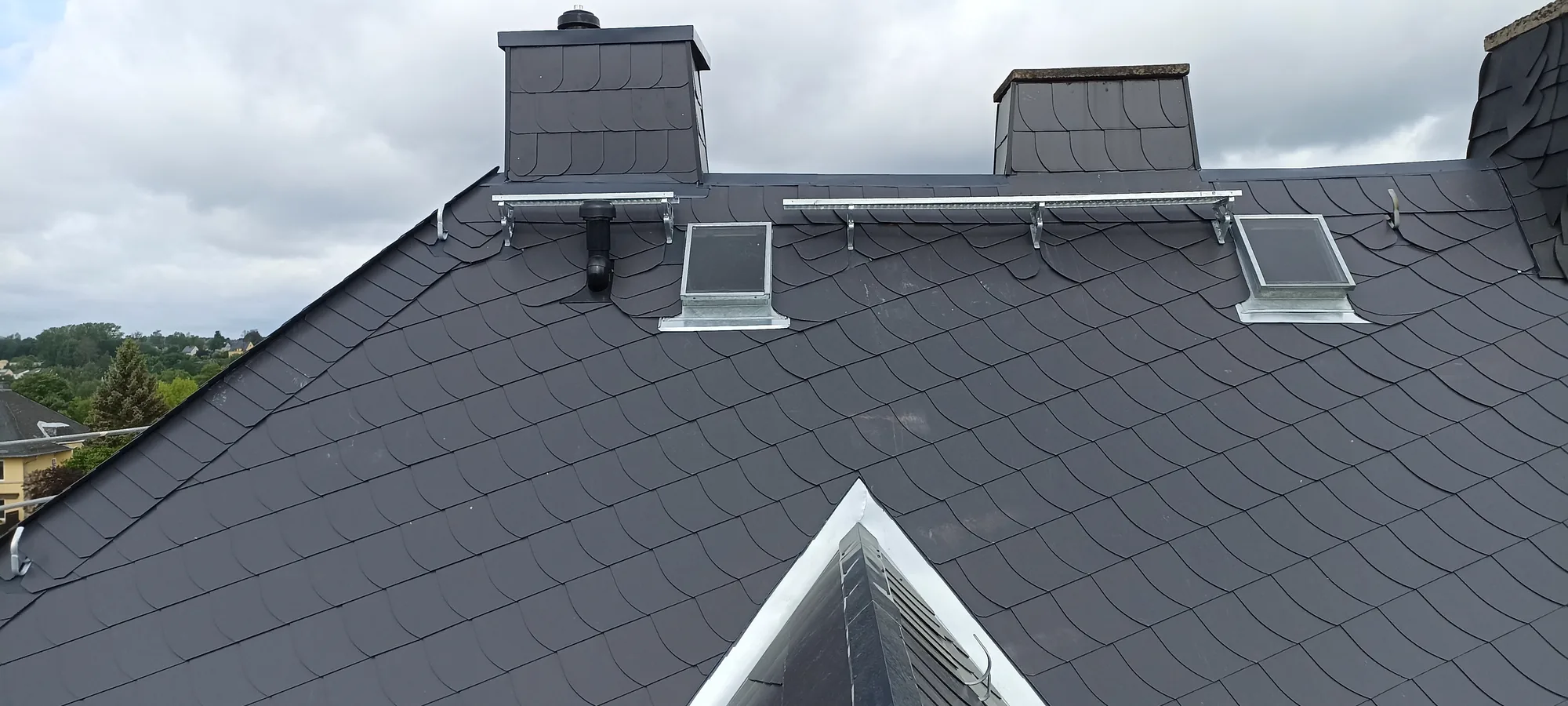 Fertiges Schieferdach mit VELUX-Dachfenstern, verschieferten Kaminen und Schneefanggitter