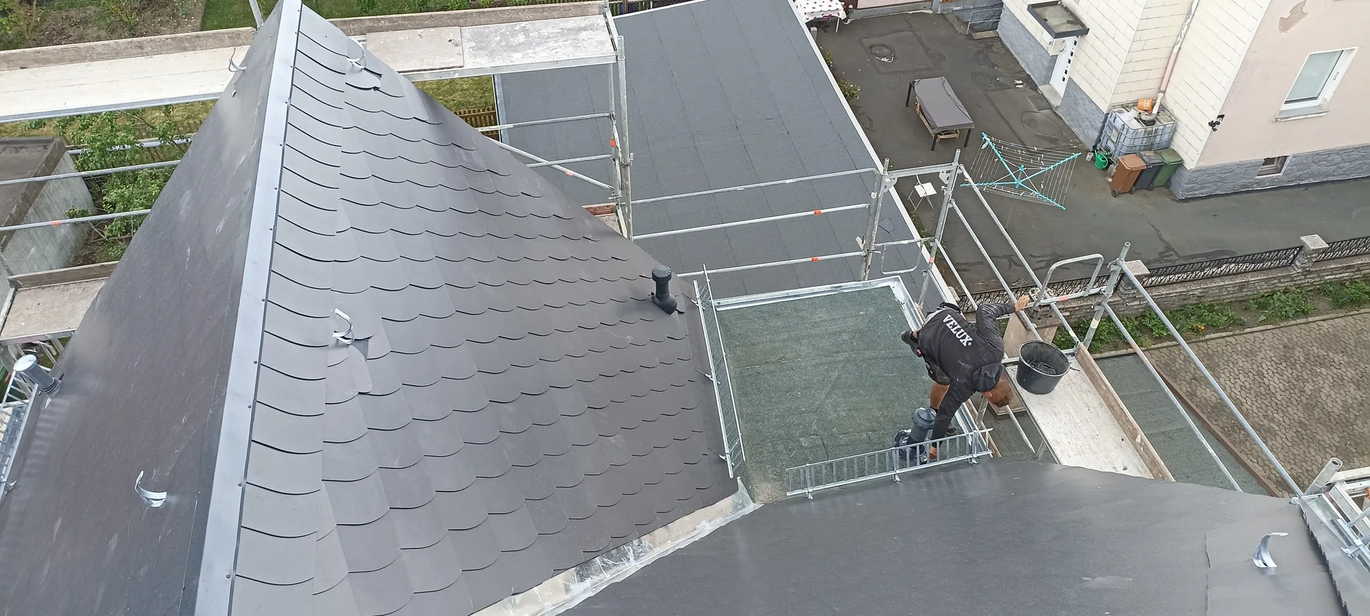 Dachdecker bei Schieferarbeiten an einer Gaube, Blick über die Dachlandschaft