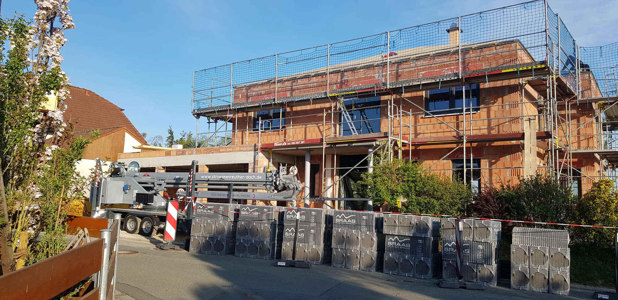 Neubau mit Baugerüst und angelieferten Dachziegeln, Kranwagen der Dachdeckerei Strößenreuther vor Ort