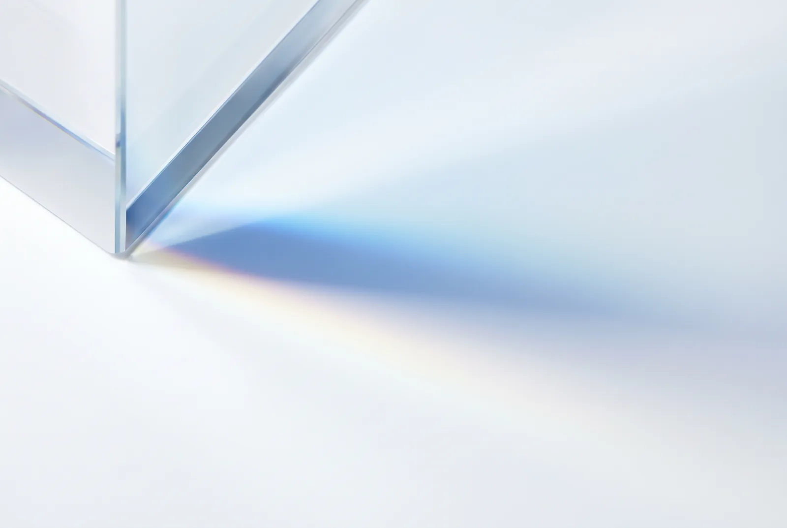 The edge of a glass prism on a white surface, splitting light into a faint spectrum, New Beach journal