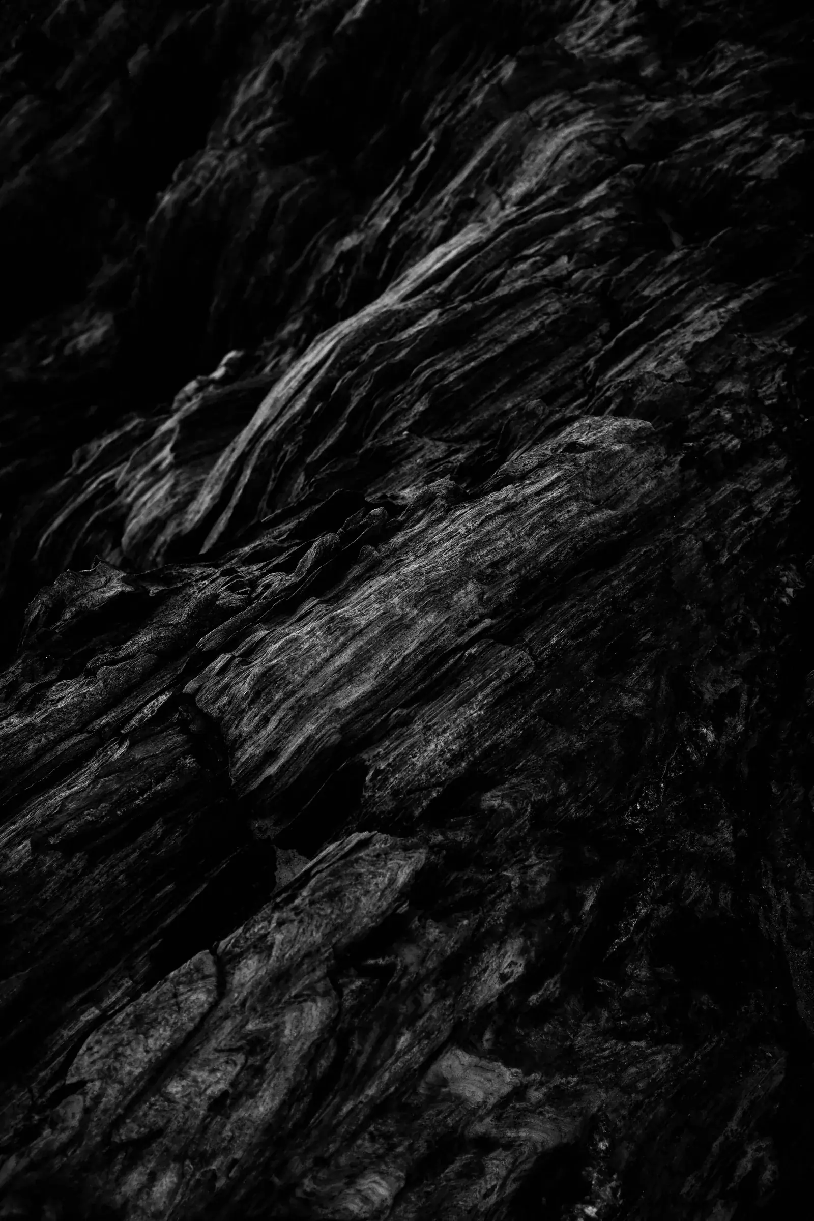 Black and white close-up of layered, striated rock catching low light, New Beach journal
