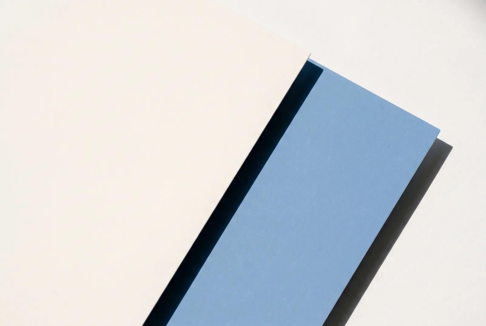 A blue rectangle of card laid on cream paper at an angle, throwing a hard dark shadow, New Beach journal