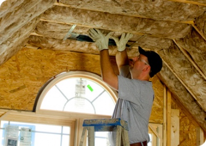 Installer fitting insulation batts in a roof space above an arched window
